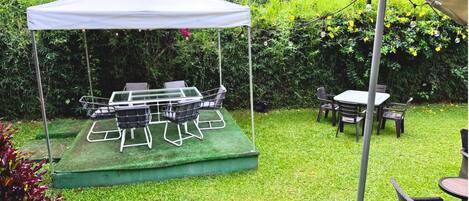 A tented outdoor seating area with a table and chairs, surrounded by lush greenery.