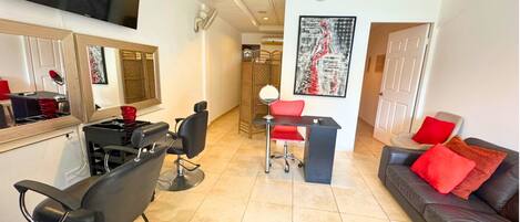 A salon with a TV, chairs, a desk, and a couch with red cushions.