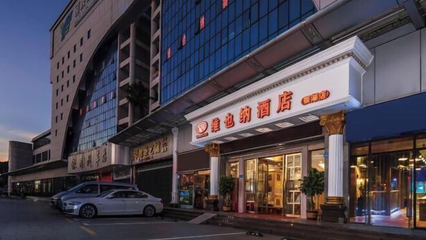 A hotel with a modern facade, large windows, and a prominent entrance with illuminated signage. - Vienna Hotel (Shenzhen Bijiashan Yinhu subway station) (Shenzhen)