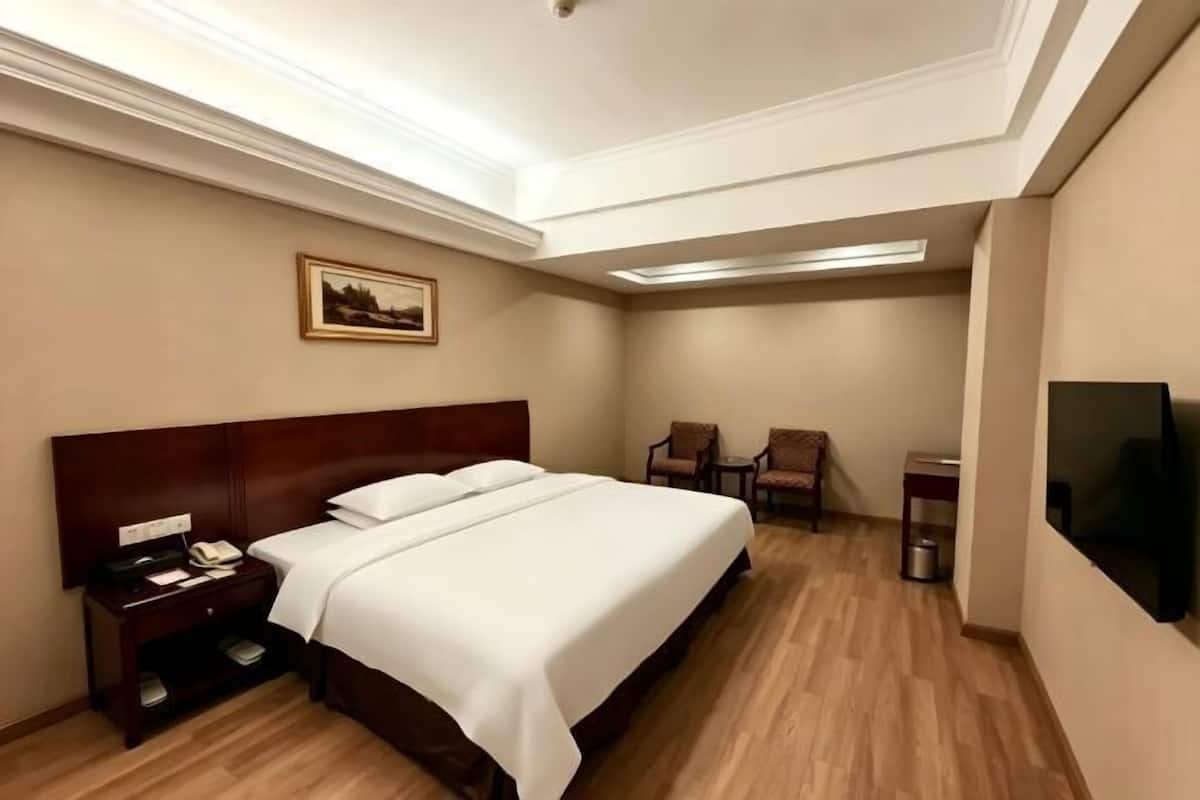 A hotel room with a large bed, a nightstand, a chair, a television, and a painting on the wall.