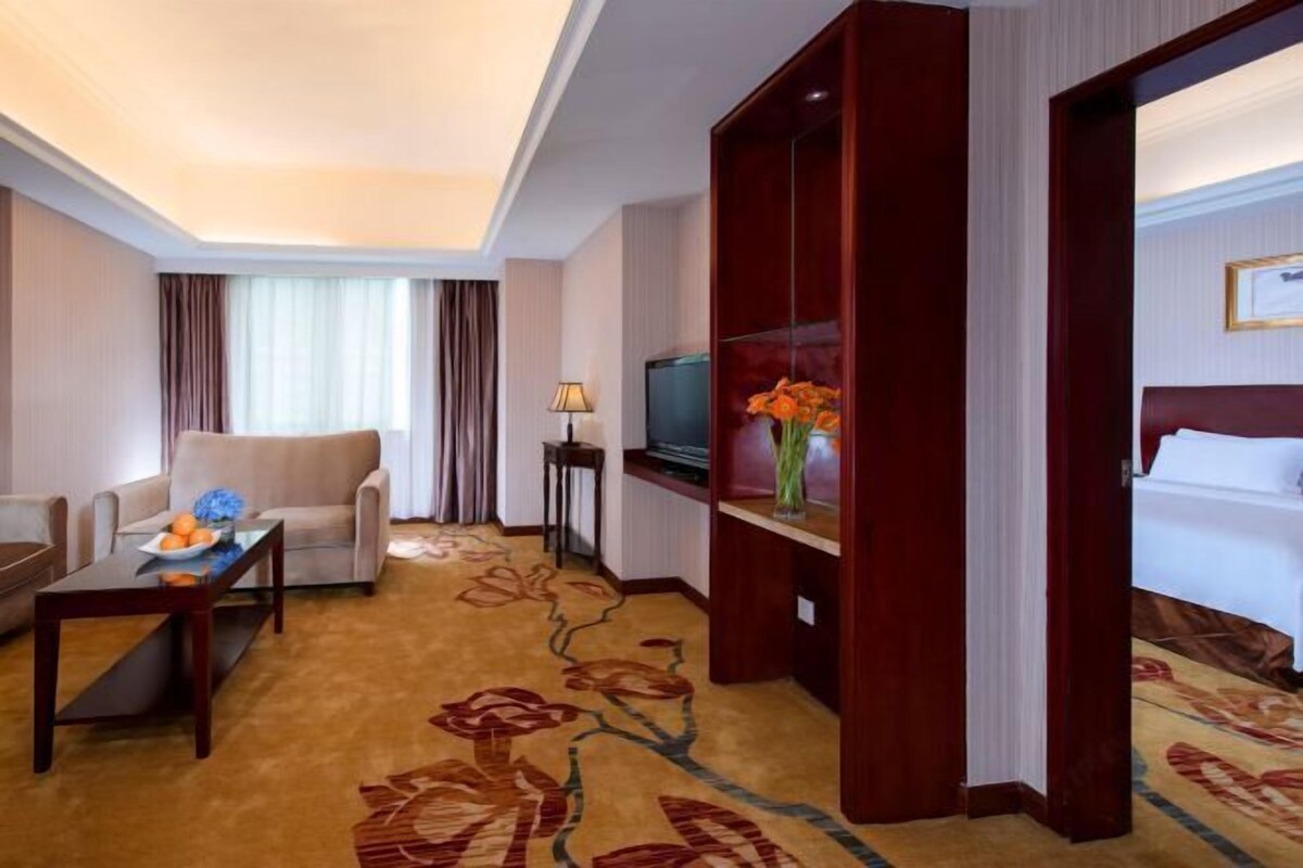 A hotel room with a sofa, a small table with fruit, a TV, a bed, and a decorative vase.