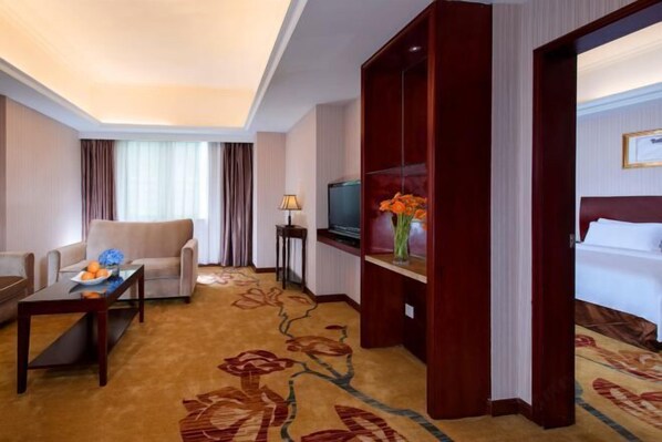 A hotel room with a sofa, a small table with fruit, a TV, a bed, and a decorative vase. - Vienna Hotel (Shenzhen Bijiashan Yinhu subway station) (Shenzhen)