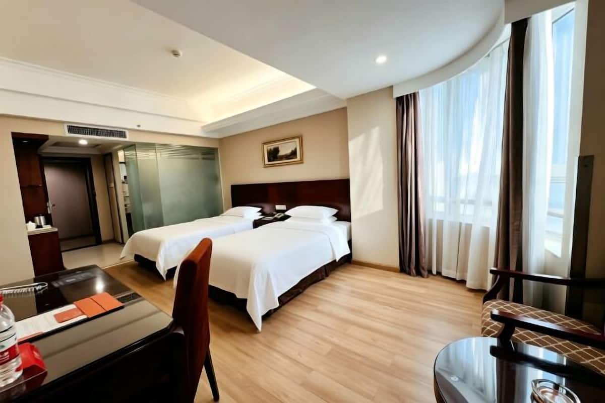 A hotel room with two beds, a desk, a chair, and a large window.