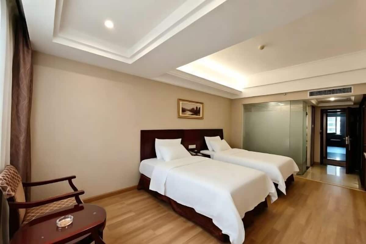 A hotel room with two beds, a wooden chair, a small table, and a mirror.