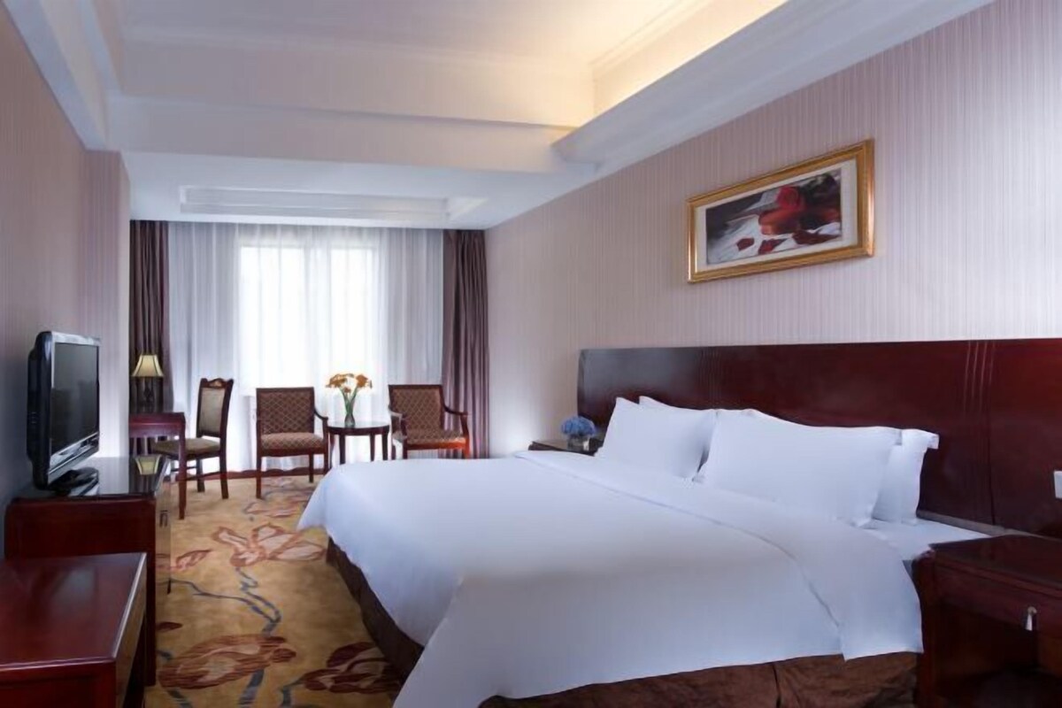 A hotel room with a large bed, a TV, a desk, and a chair.