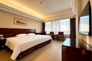 Une chambre d’hôtel avec un grand lit, un bureau, une chaise, une télévision et une fenêtre avec des rideaux.