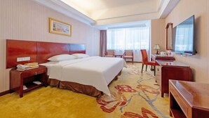 A hotel room with a large bed, a desk, a chair, a television, and a window with curtains. - Vienna Hotel (Shenzhen Bijiashan Yinhu subway station) (Shenzhen)