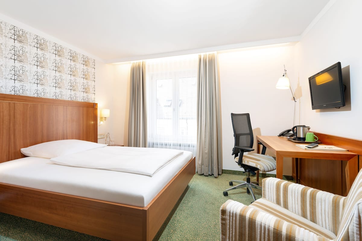 A hotel room with a wooden bed, a desk with a chair, a television, and a window with curtains.