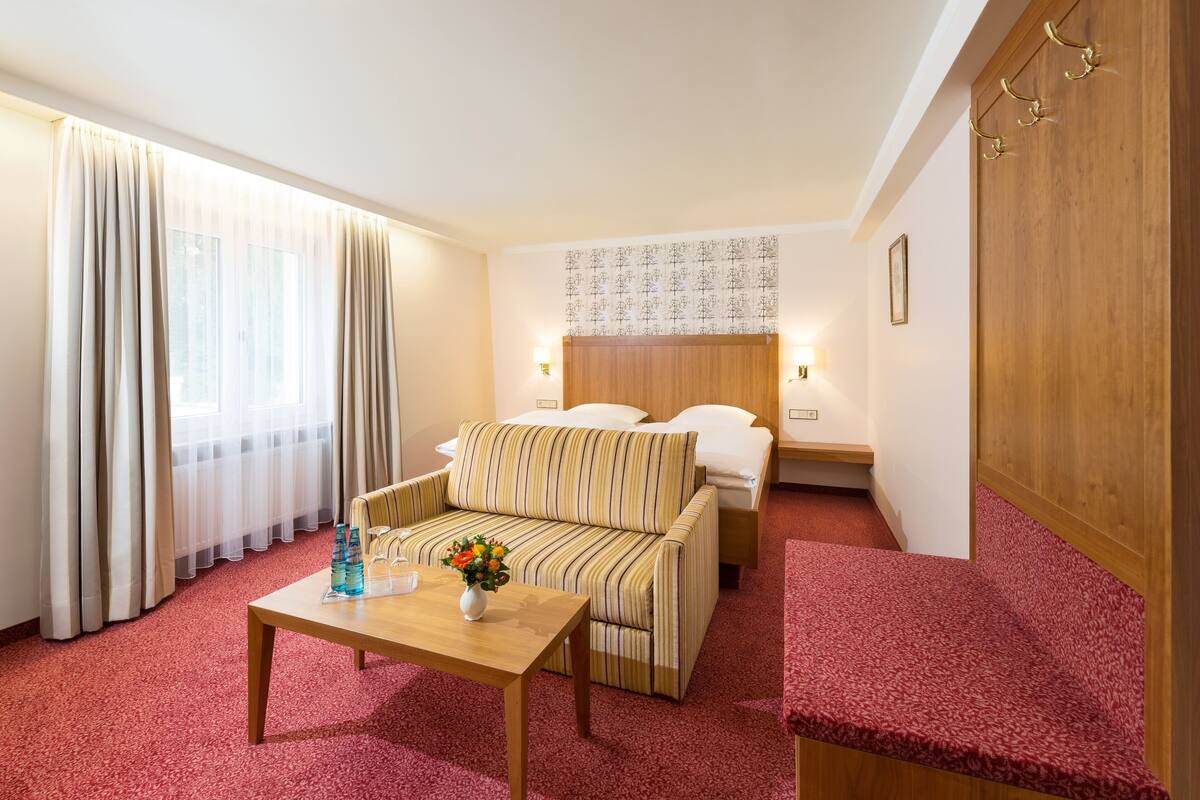 A hotel room with a bed, a sofa, a wooden table, and a red carpet.