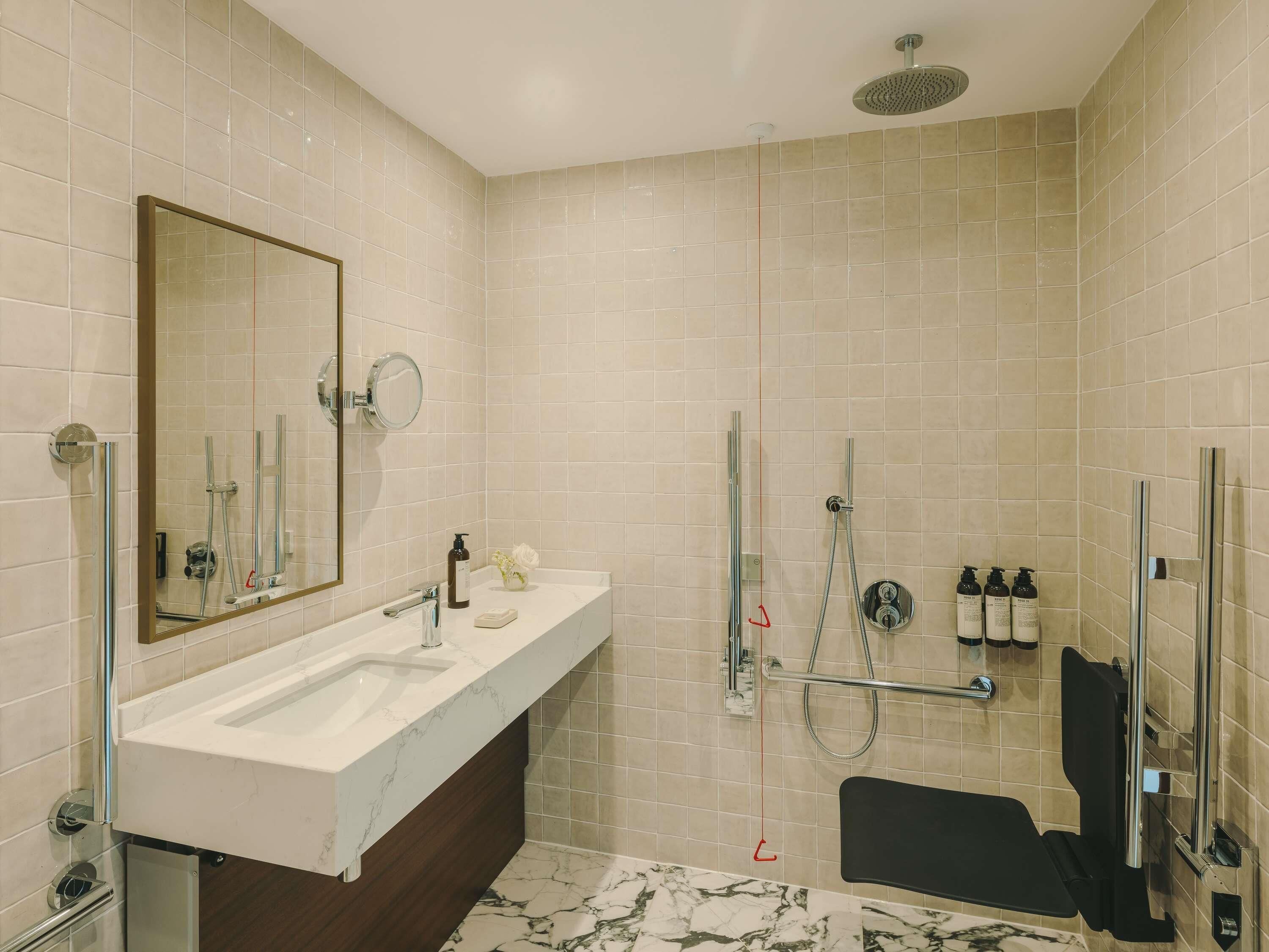 Un bagno moderno con un grande specchio, due lavabi, una doccia e una panca nera.