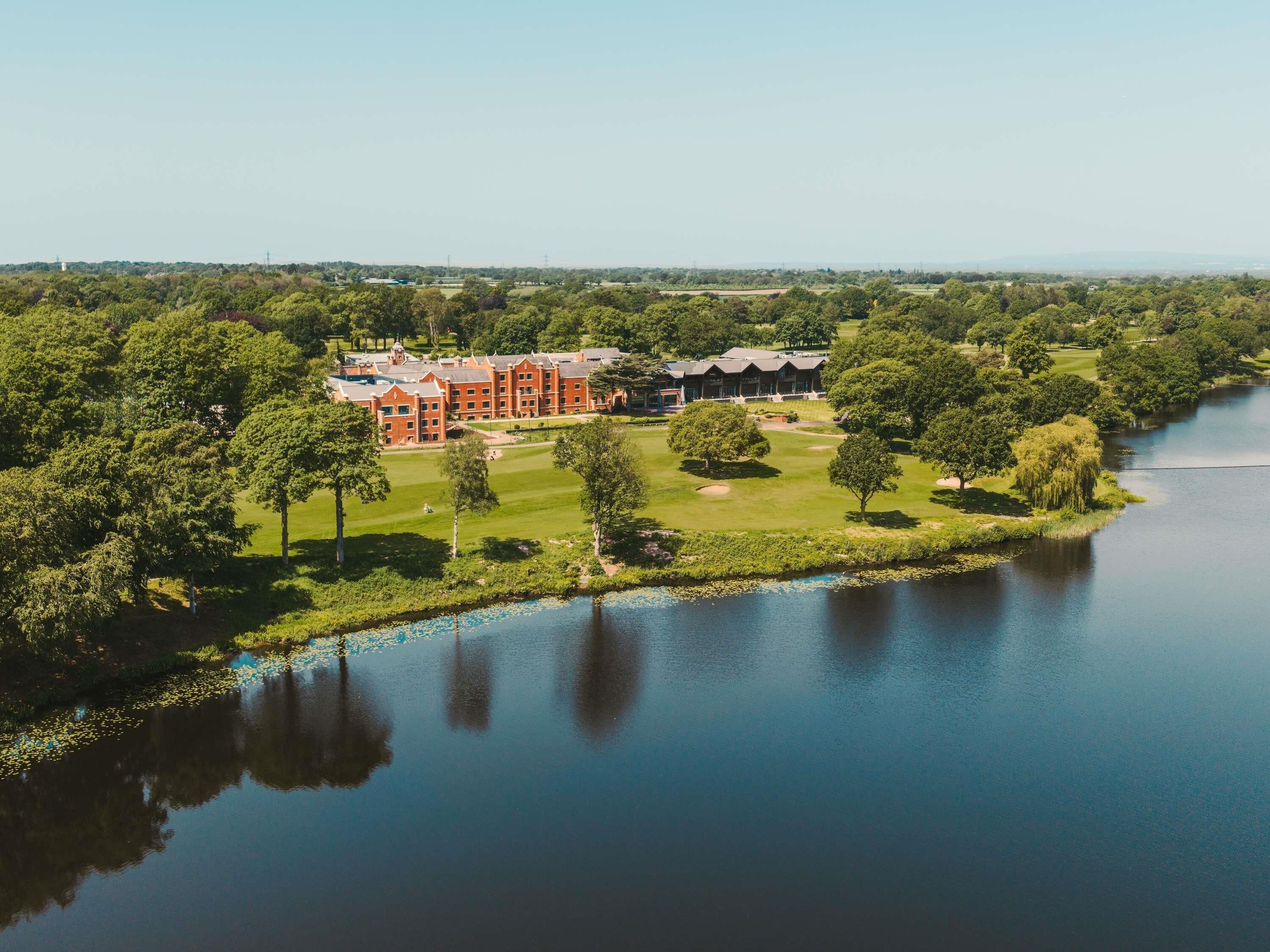 A large building complex with multiple structures, surrounded by lush greenery and a body of water.