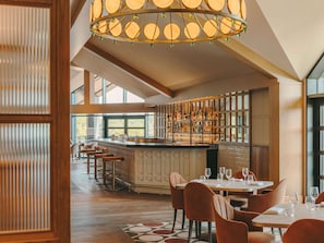 A modern restaurant with a bar area, high ceilings, and large windows. - Fairmont Cheshire The Mere (Opening July 2026) (Knutsford)