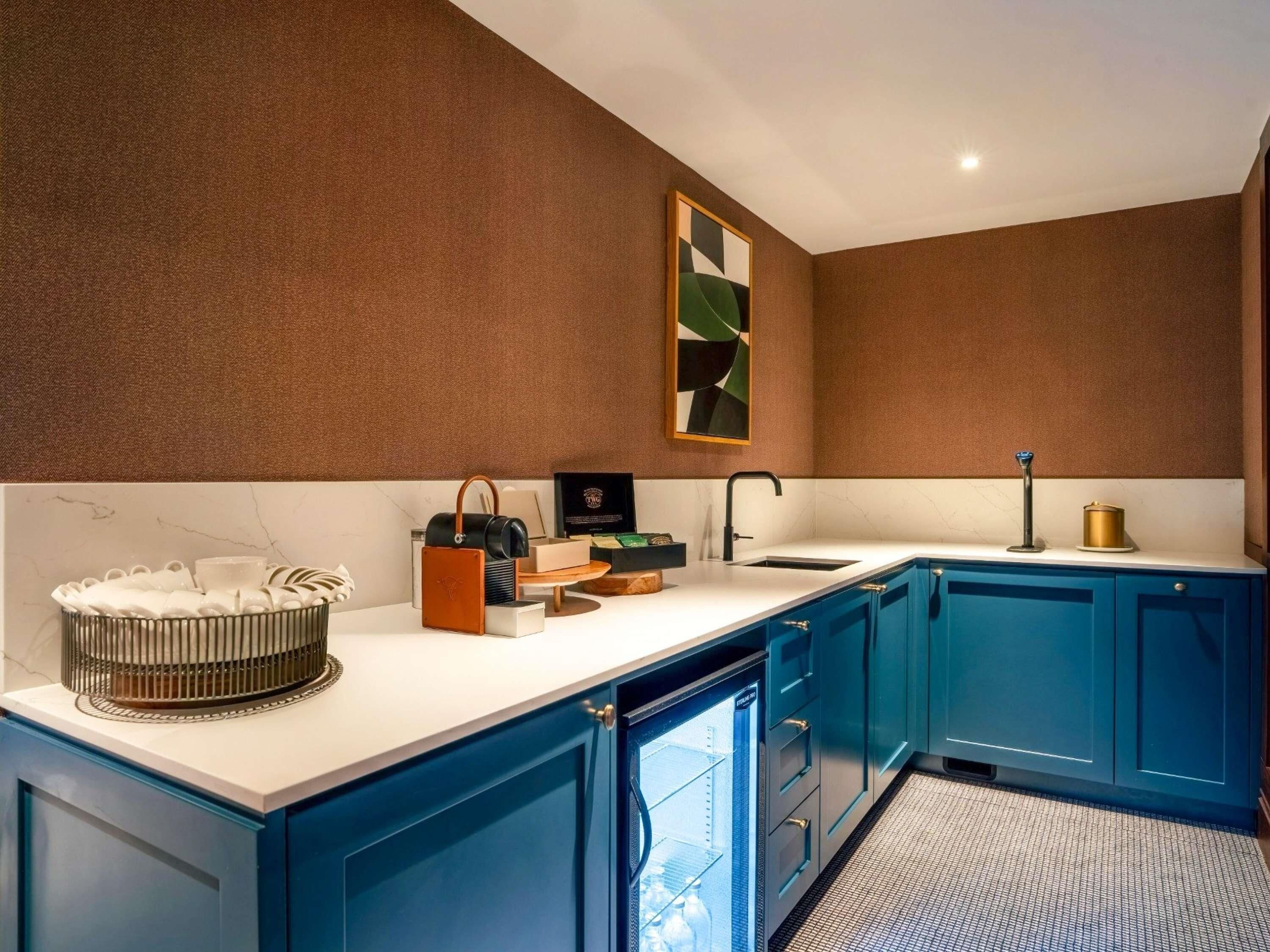 A modern kitchen with blue cabinets, a marble countertop, and a stainless steel refrigerator.