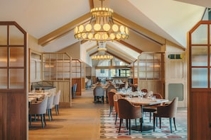 Un restaurante con paneles de madera, varias mesas de comedor y candelabros colgantes.