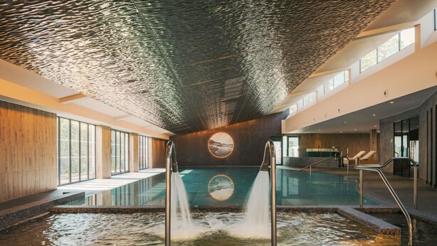 An indoor swimming pool with a tiled border, a circular skylight, and a view of the outdoors through large windows. - Fairmont Cheshire The Mere (Knutsford)