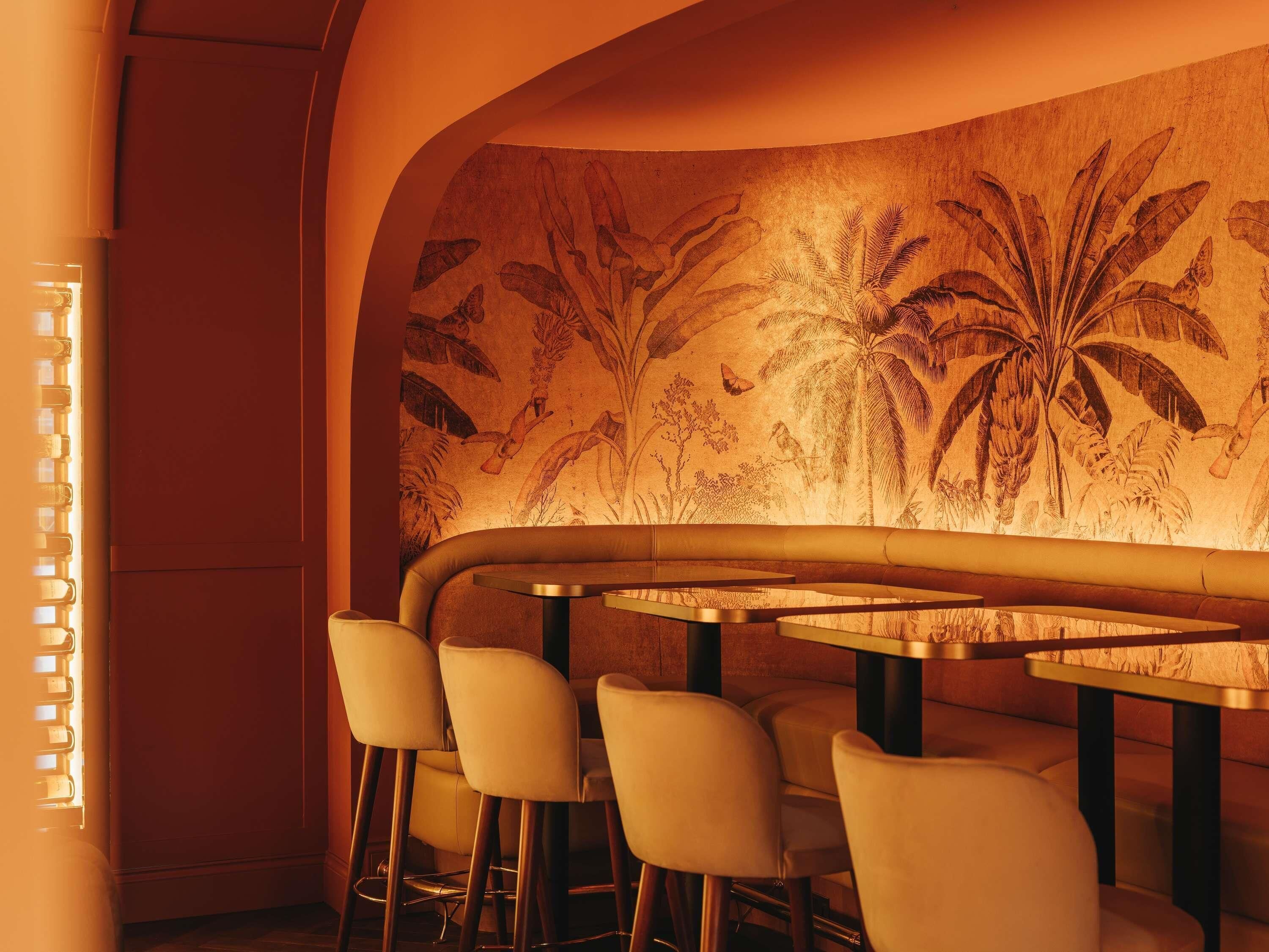 A restaurant interior with a curved wall mural, round tables, and bar stools.
