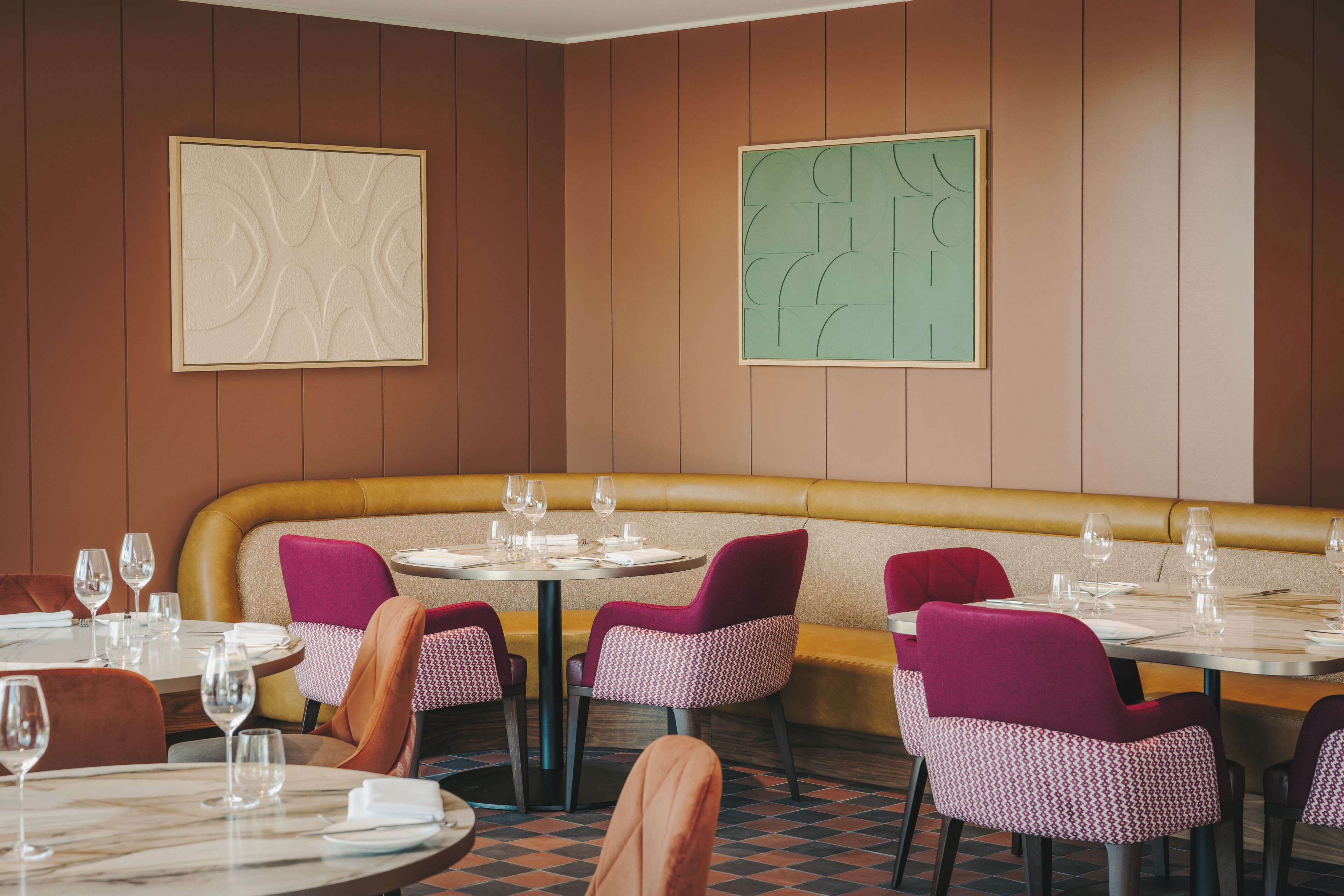 Un restaurant avec des banquettes, des tables rondes et des chaises.