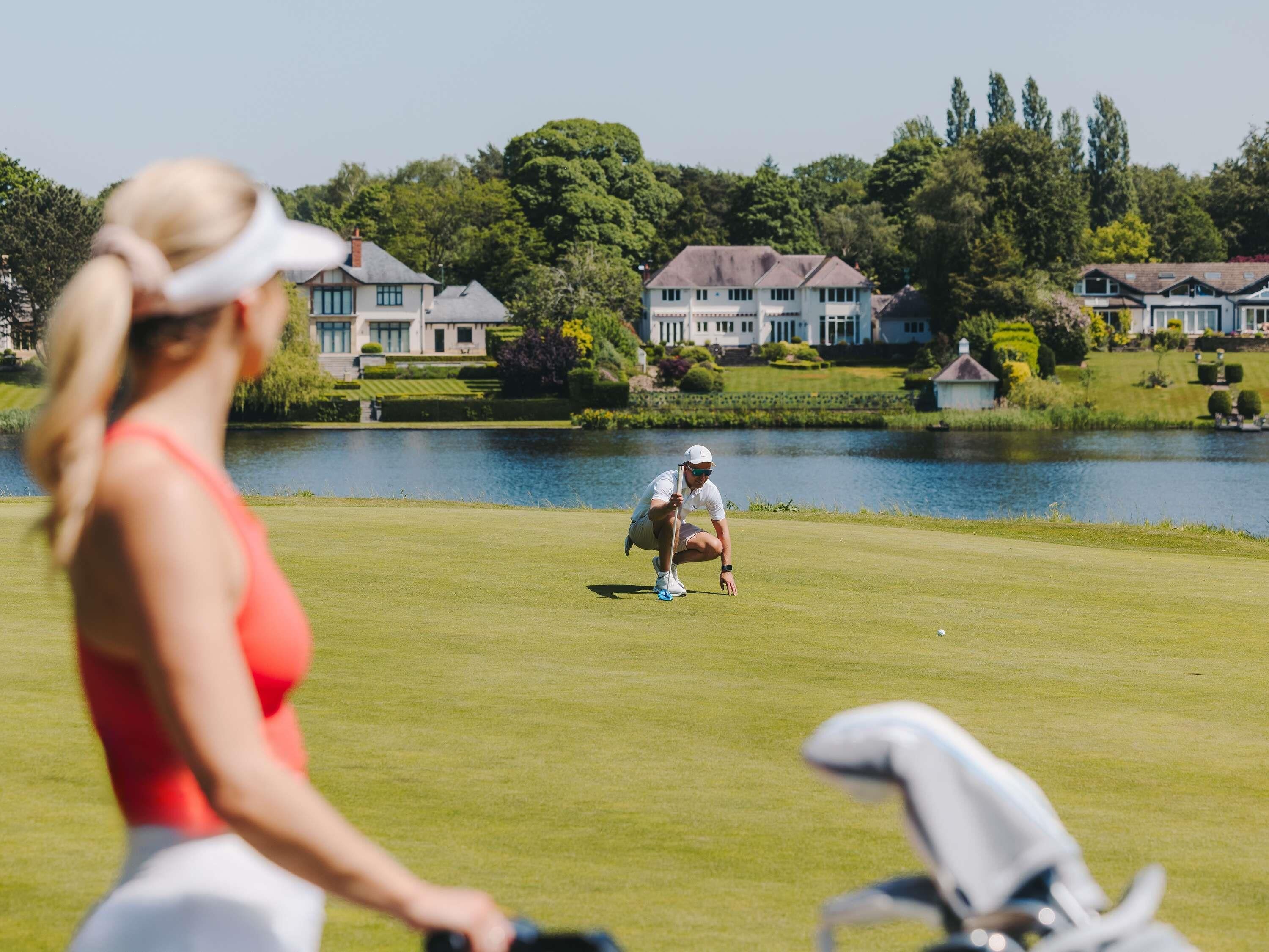 Un campo de golf con un lago, casas y árboles al fondo.