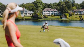 Un campo de golf con un lago, casas y árboles al fondo.
