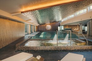 Un área de piscina interior moderna con una fuente central, asientos y un amplio ventanal que proporciona luz natural.