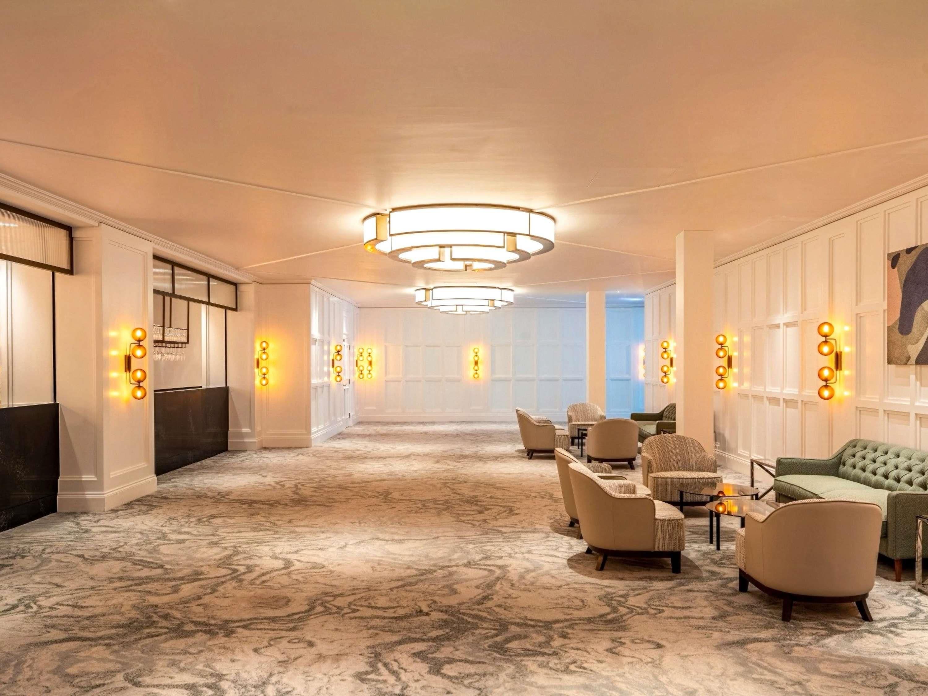 A hotel lobby with a marble floor, seating area with armchairs and sofas, and wall sconces with lights.