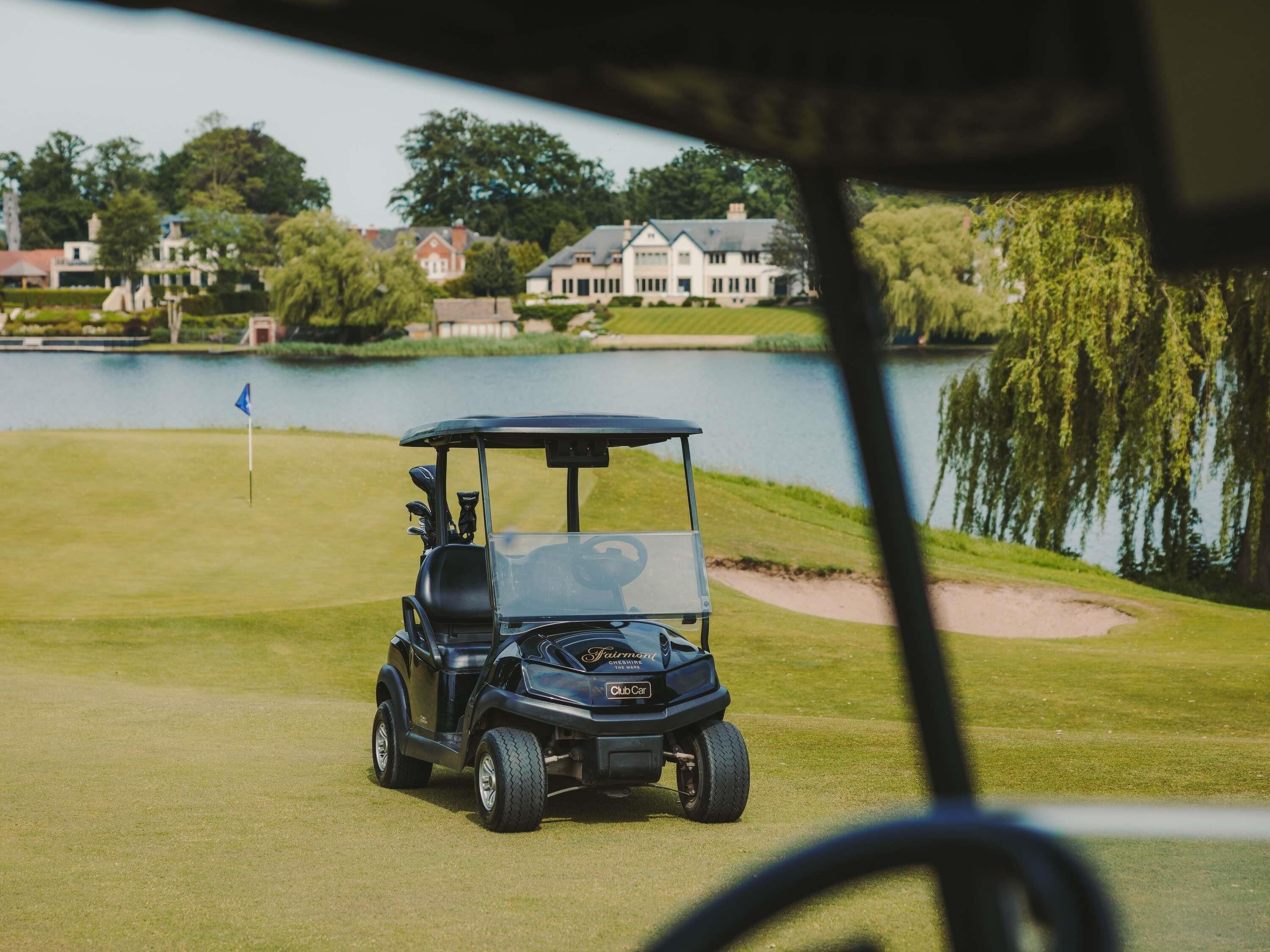 Une voiturette de golf sur un terrain de golf, avec un lac et des maisons en arrière-plan.
