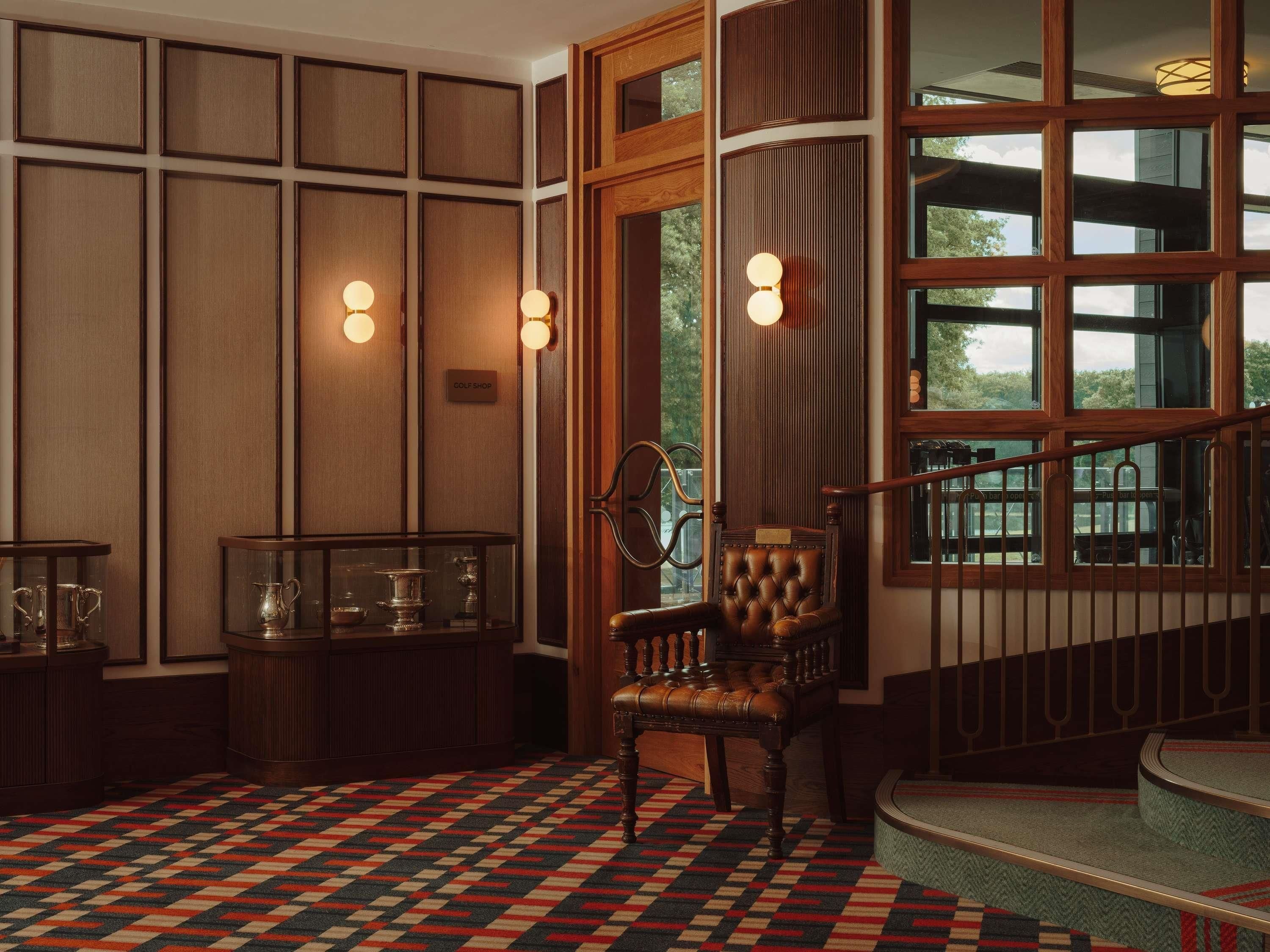 A room with a patterned carpet, a wooden chair, a glass display case, and a window with a view of greenery.