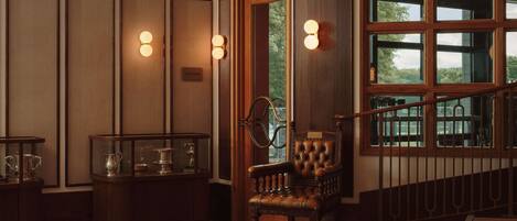 A room with a patterned carpet, a wooden chair, a glass display case, and a window with a view of greenery.