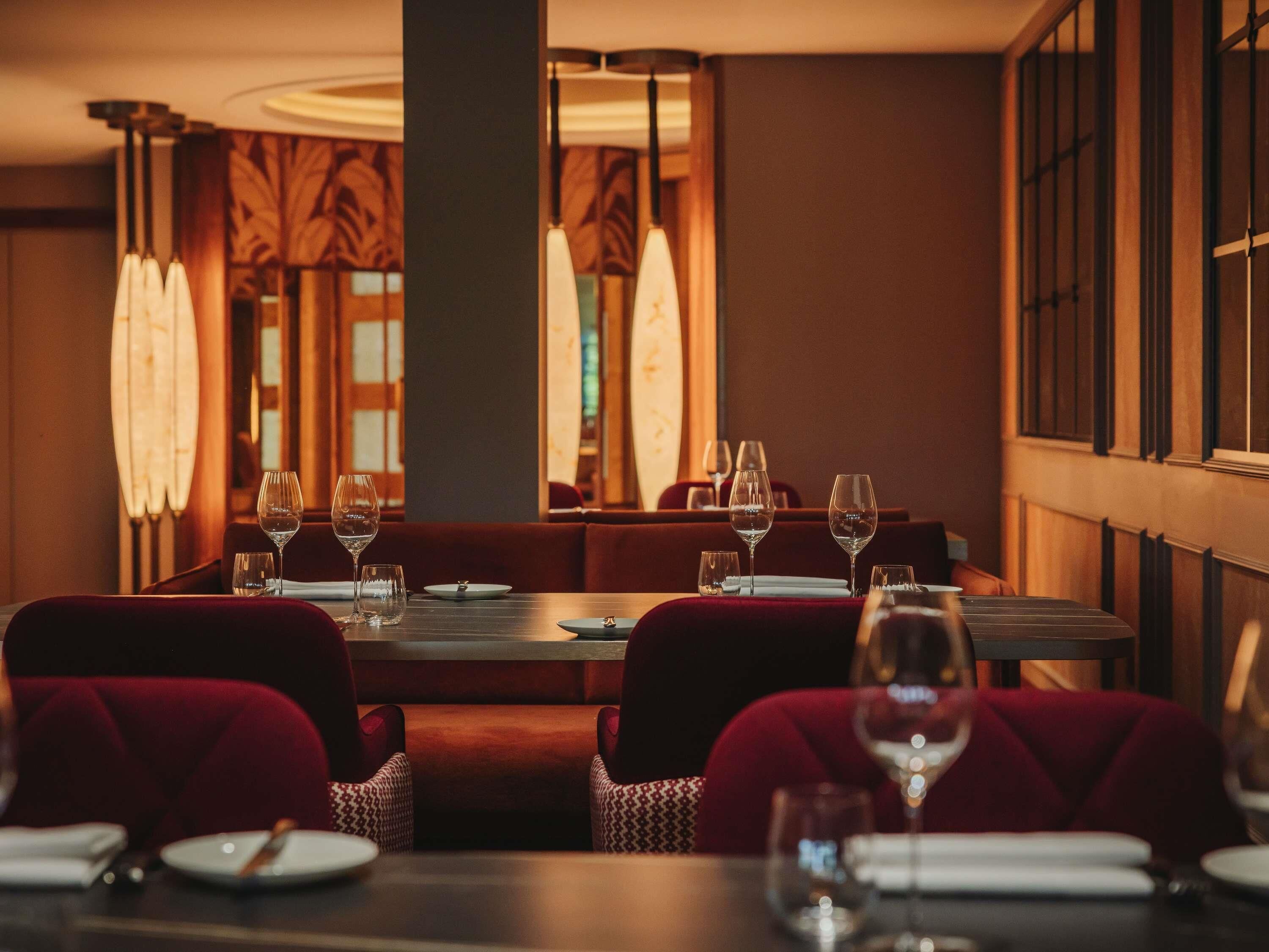 A restaurant with a long table, red upholstered chairs, and hanging pendant lights.