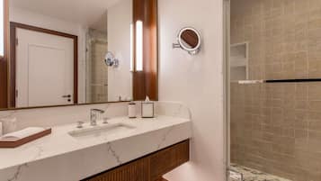 Un baño con un espejo grande, un lavamanos, un perchero para toallas y una zona de ducha.