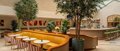 A spacious indoor area with a high ceiling, a seating area with yellow sofas and round tables, and a bar counter.