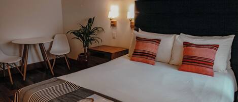 A hotel room with a bed, a small table, two chairs, a plant, and wall-mounted lights.