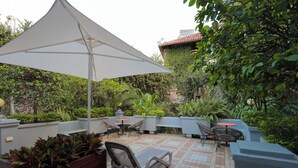 Eine Terrasse im Freien mit einem weißen Sonnenschirm, Liegestühlen und einem Fliesenboden.