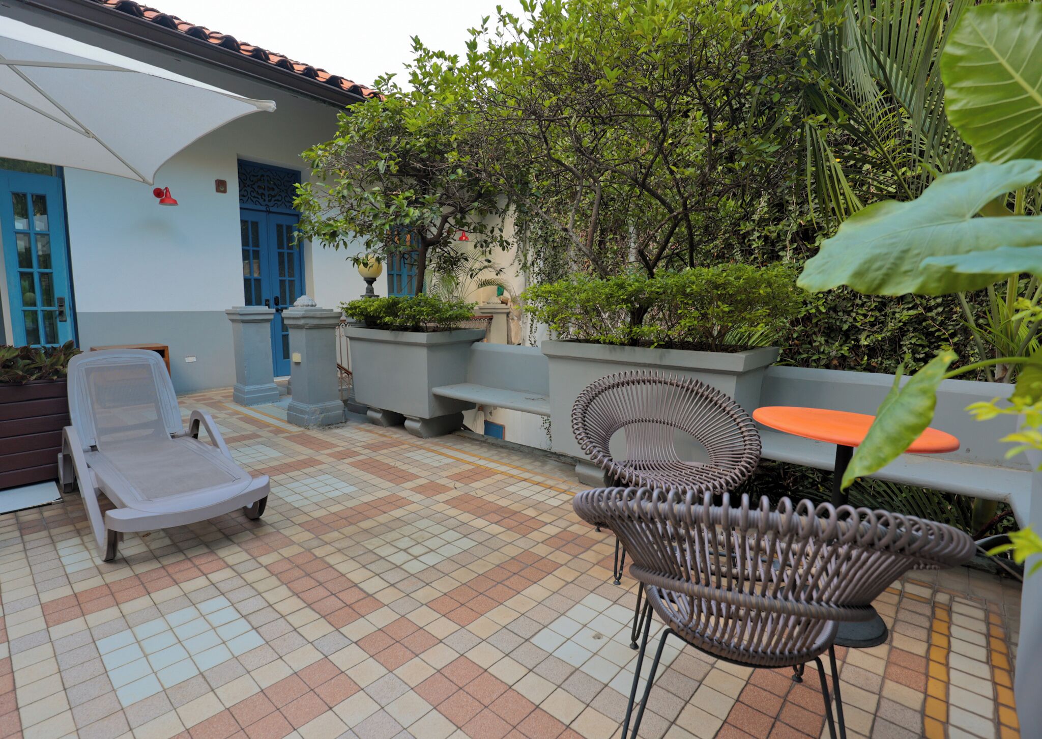 Een terras met betegelde vloer, een lounge stoel, een rieten stoel en een tafel.