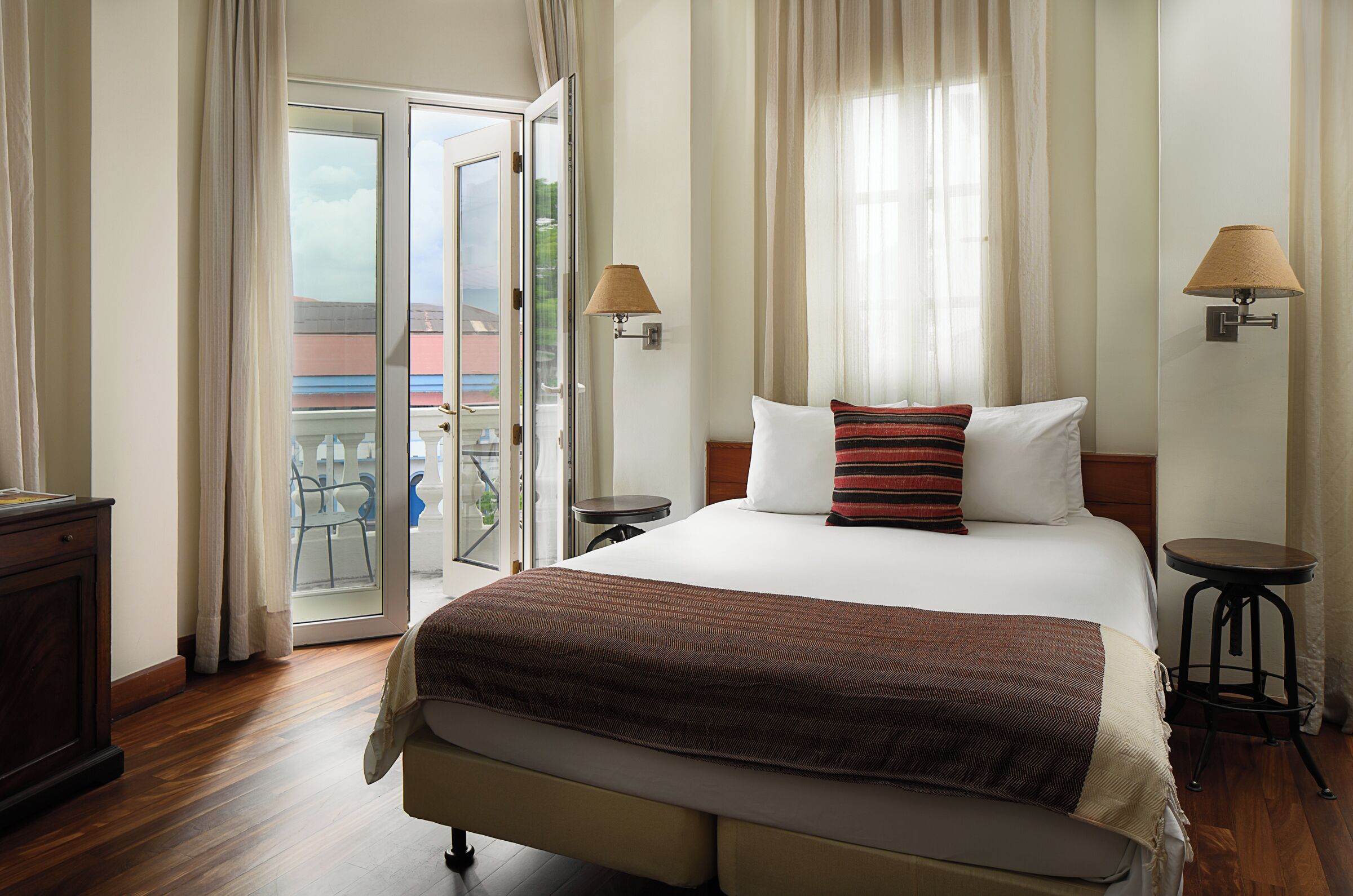 Een hotelkamer met een bed, twee nachtkastjes, een lamp, een raam met gordijnen en uitzicht op het omliggende landschap.