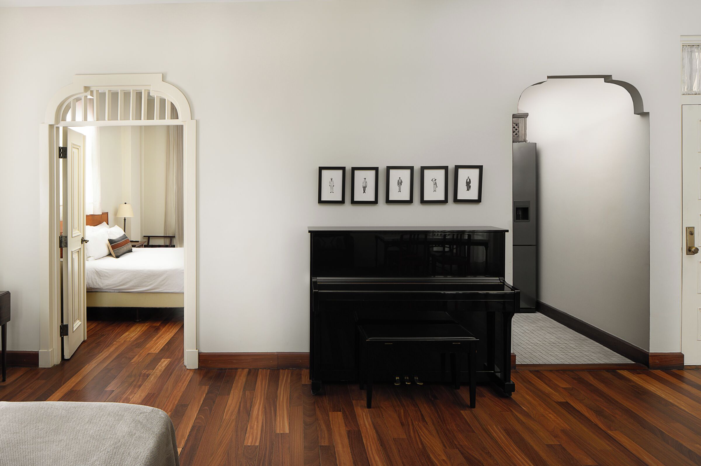 A room with a bed, a piano, and framed pictures on the wall.
