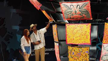 Un hombre y una mujer de pie frente a una exhibición de tapices coloridos sobre un fondo negro.
