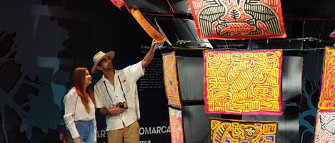 A man and a woman standing in front of a display with colorful tapestries and a black background.