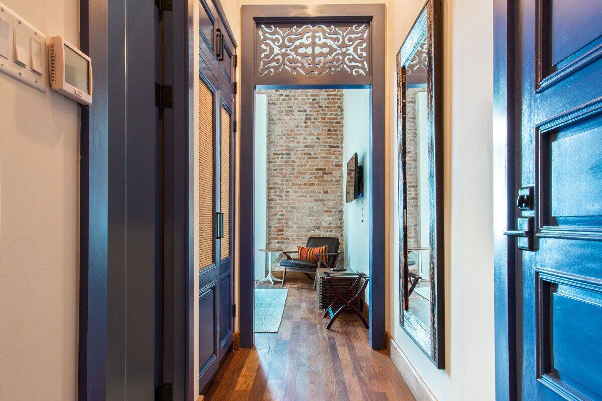 A hallway with a brick wall, a blue door, and a chair with a cushion.
