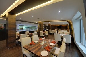 Um restaurante moderno com mesa de madeira posta para refeição, rodeada por cadeiras brancas.