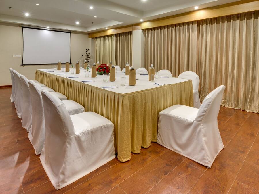 Una sala de conferencias con una mesa larga, sillas blancas y una pantalla para proyector.
