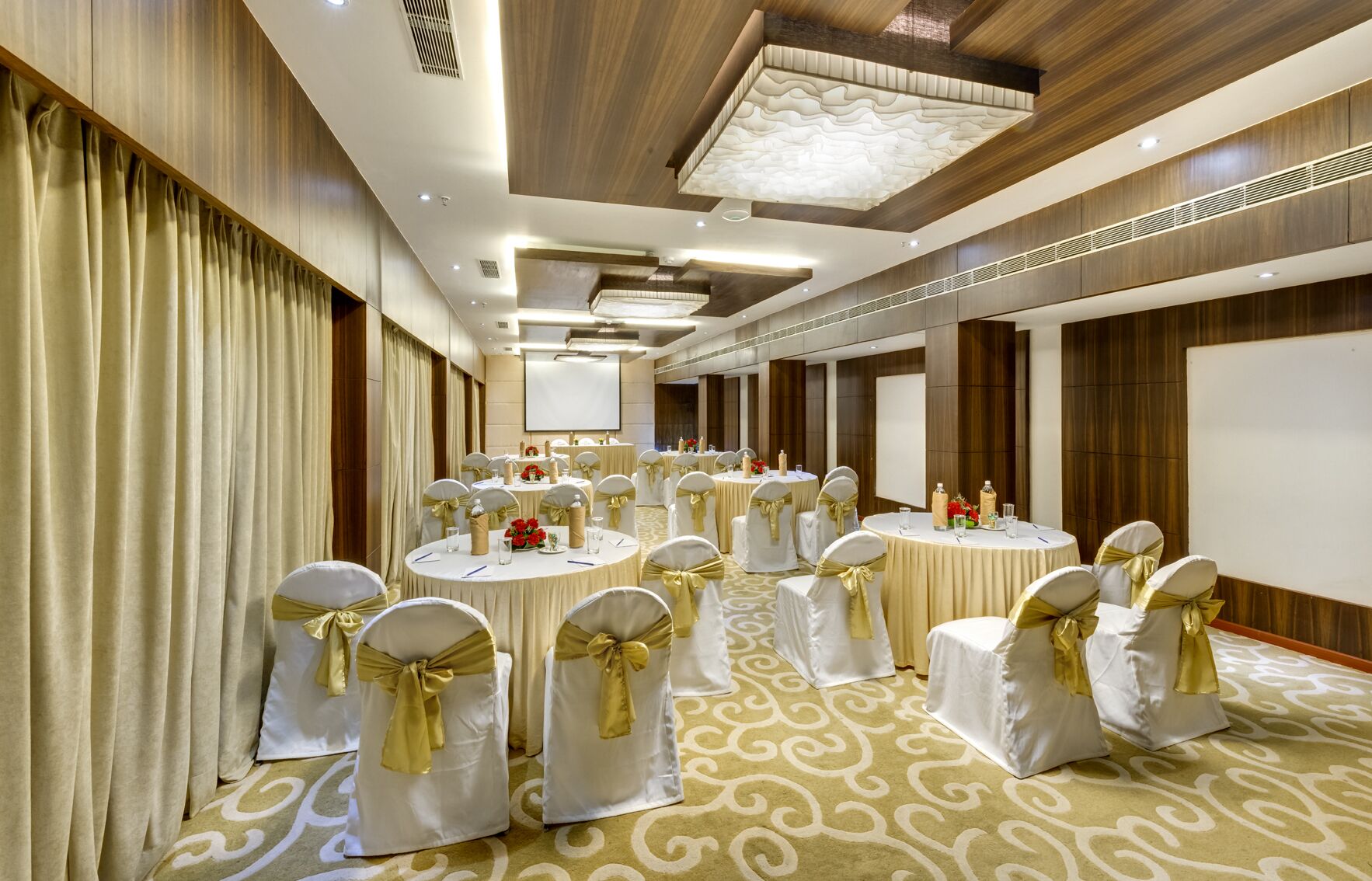 A conference room with round tables, white chairs with gold sashes, and a patterned carpet.