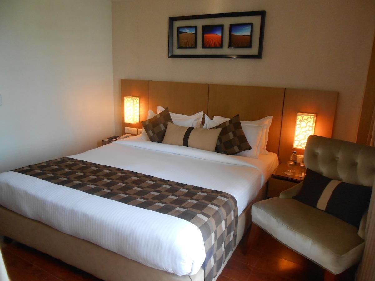 A hotel room with a large bed, a chair, two bedside tables, and a framed picture above the bed.