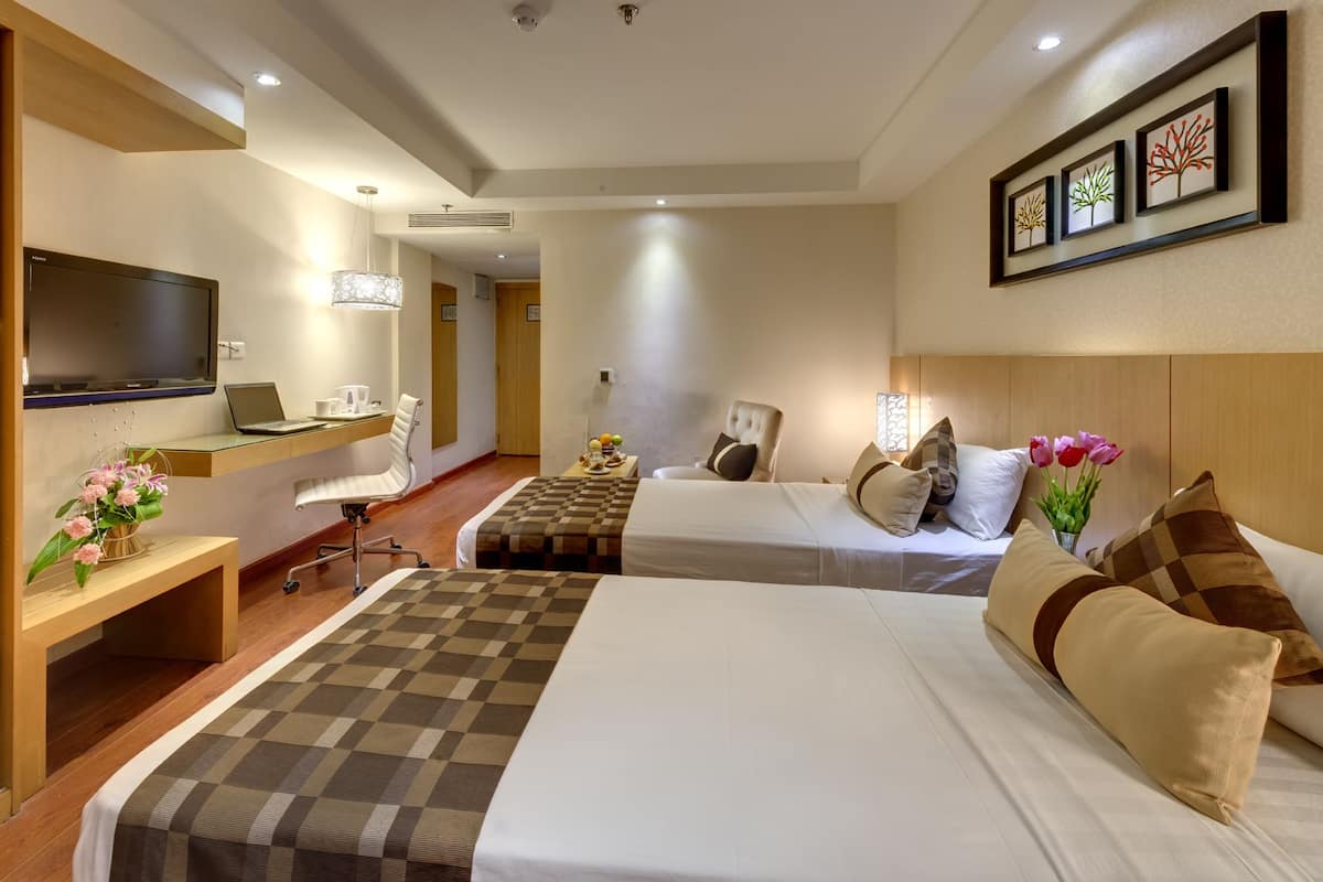 A hotel room with two beds, a desk, a chair, a TV, and artwork on the wall.