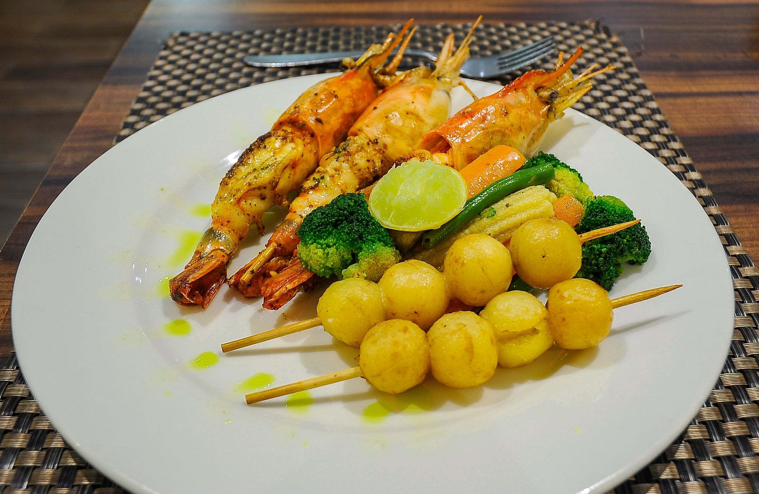 A plate with grilled shrimp, broccoli, and yellow vegetable skewers.