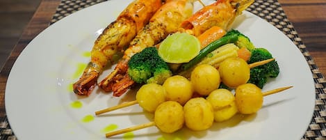 A plate with grilled shrimp, broccoli, and yellow vegetable skewers.