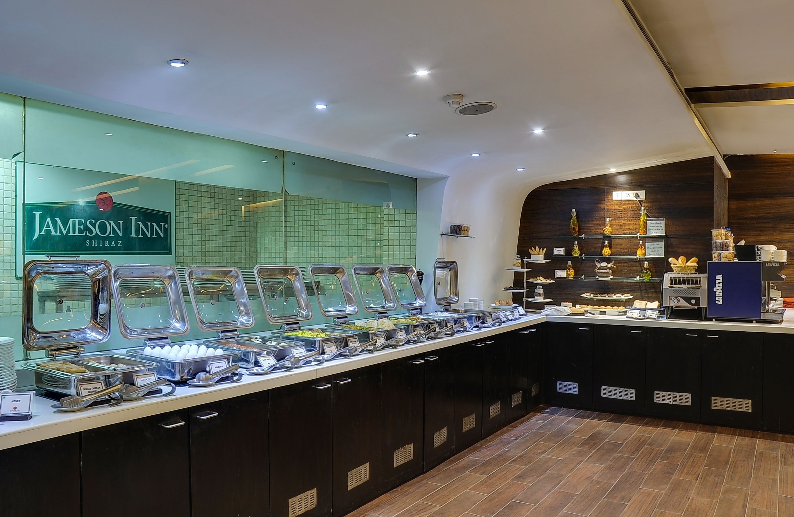 A buffet area with multiple food dispensers, a coffee machine, and a sign for Jameson Inn Shiraz.