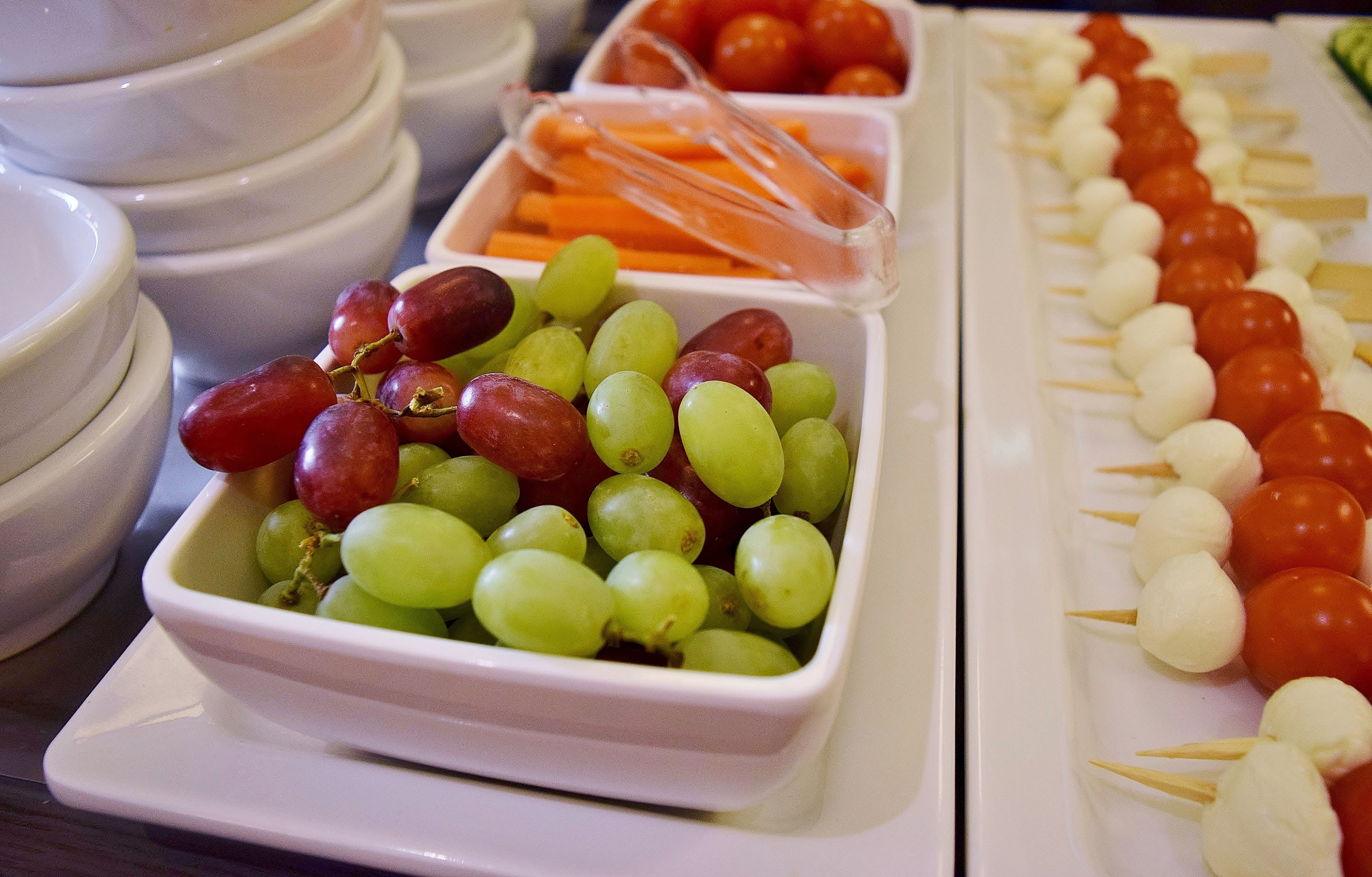 Un bufé con distintos alimentos, entre ellos uvas, tomates cherry y brochetas.
