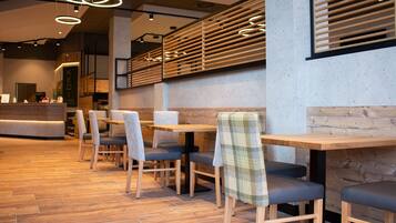 A modern restaurant interior with wooden tables and chairs, a reception desk, and a concrete wall with wooden slats.