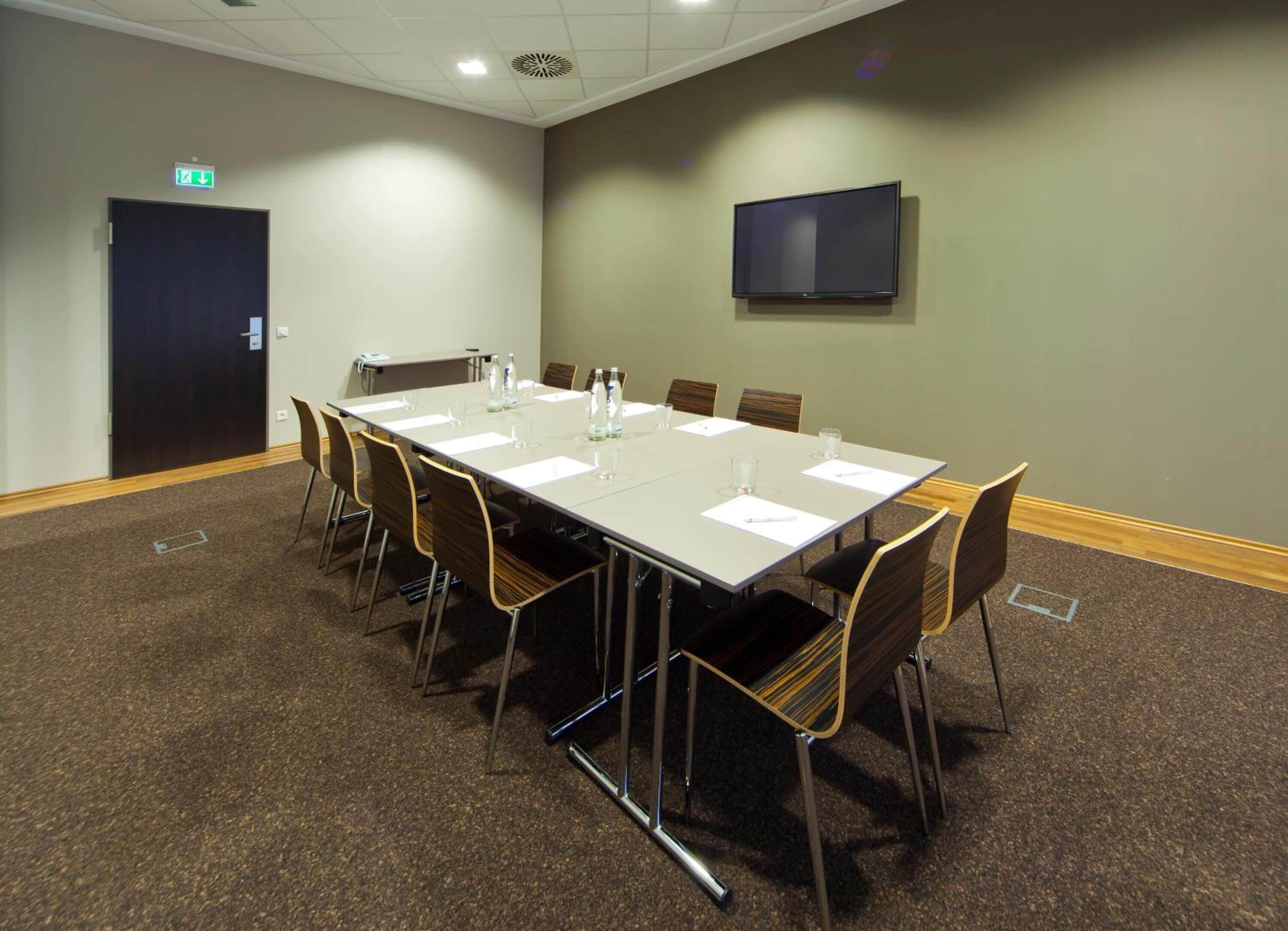 A conference room with a long table, chairs, water bottles, and a TV on the wall.